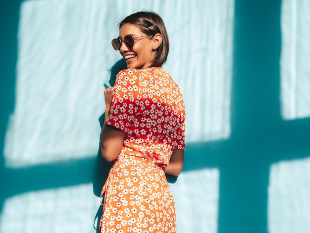 Jonge mooie lachende vrouw in trendy zomer rode jurk Sexy zorgeloze vrouw poseren in de buurt van blauwe muur in studio Positief model plezier vrolijk en gelukkig op zonnige dag schaduw van raam