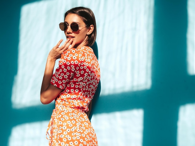 Jonge mooie lachende vrouw in trendy zomer rode jurk Sexy zorgeloze vrouw poseren in de buurt van blauwe muur in studio Positief model plezier vrolijk en gelukkig op zonnige dag schaduw van raam