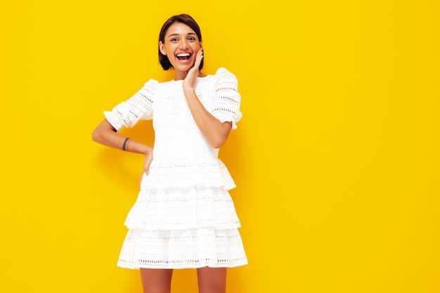 Jonge mooie lachende vrouw in trendy zomer witte jurk Sexy zorgeloze vrouw poseren in de buurt van gele muur in studio Positief model plezier vrolijk en gelukkig geïsoleerd