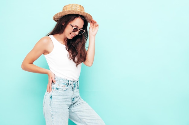 Jonge mooie lachende vrouw in trendy zomerkleren Sexy zorgeloze vrouw poseren in de buurt van blauwe muur in studio Positieve brunette model plezier vrolijk en gelukkig In hoed