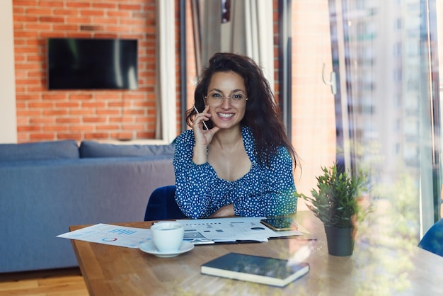 Jonge mooie lachende vrouw op bril met tablet pc en zakelijke documenten zittend op tafel bij