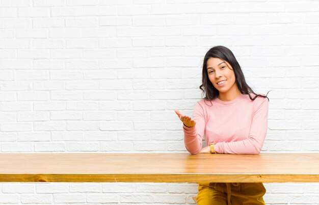 Jonge mooie Latijns-vrouw die lacht, er blij, zelfverzekerd en vriendelijk uitziet, een handdruk aanbiedt om een deal te sluiten, samenwerkend voor een tafel