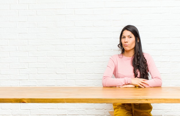 Jonge mooie Latijns-vrouw voelt zich verward en twijfelachtig, vraagt zich af of probeert te kiezen of een beslissing te nemen voor een tafel