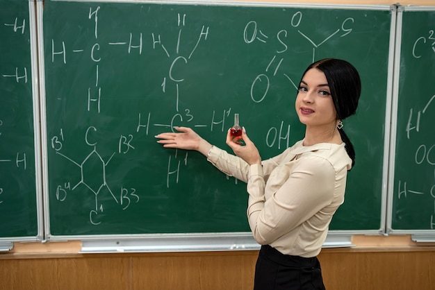 Jonge mooie leraar leert les over scheikunde en staat in de buurt van bord met chemische formule, onderwijsconcept