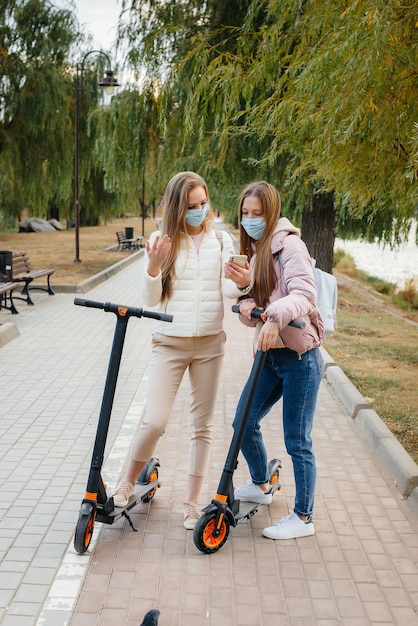 Jonge mooie meisjes in maskers rijden in het Park op een elektrische scooter op een warme herfstdag en nemen selfies