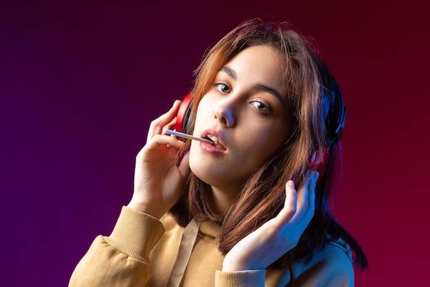 Jonge mooie modieuze hipster meisje gekleed in een hoodie luisteren naar muziek in rode koptelefoon in een studio rode dramatische achtergrond