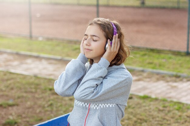 Jonge mooie modieuze tiener meisje luistert naar muziek op koptelefoon van een smartphone