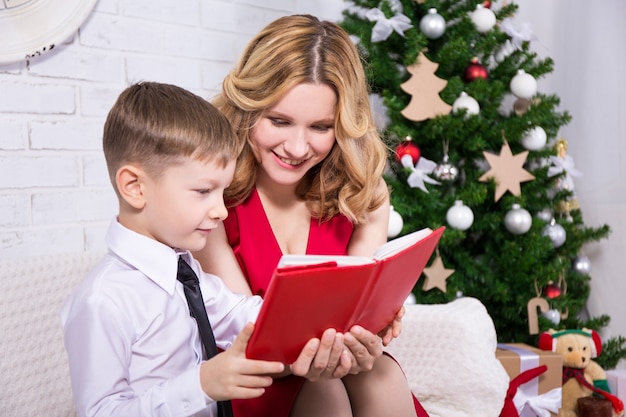 Jonge, mooie moeder die een boek leest aan zijn zoon voor de kerstboom