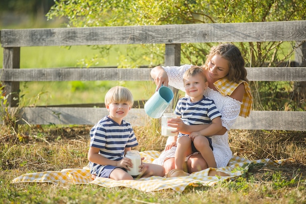 Jonge mooie moeder die picknick met haar kleine kinderen heeft. Familie consumptiemelk buitenshuis