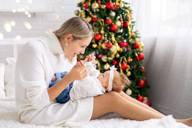 Jonge mooie moeder en baby die Kerstmis thuis vieren met een kerstboom en versieringen