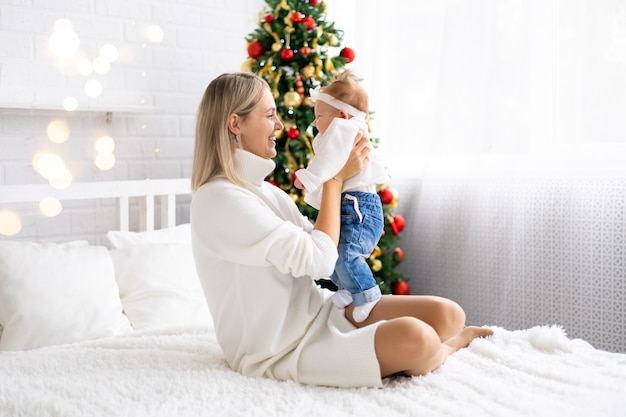 Jonge mooie moeder en baby die Kerstmis thuis vieren met een kerstboom en versieringen