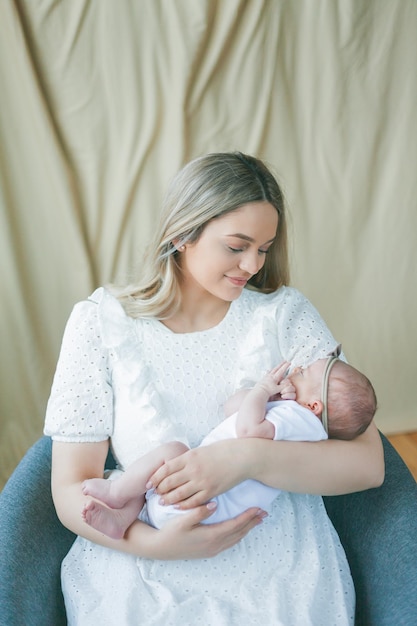 Jonge mooie moeder met blauwe ogen houdt haar pasgeboren dochtertje in haar armen Motherhood Care Baby