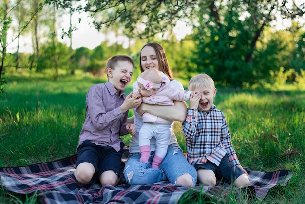 Jonge mooie moeder met dochter en twee zonen op plaid in het park. Kindergelach, gelukkige jeugd