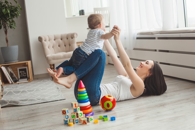 Jonge mooie moeder speelt met haar zoontje. Vrolijke familie plezier binnenshuis met kleine baby zoon