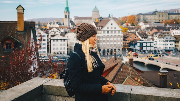 Jonge mooie mooie blonde toeristische meisje in warme muts en jas met rugzak wandelen in de koude herfst in Europa stad genieten van haar reizen in Zürich, Zwitserland