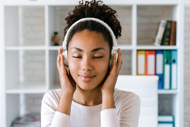 Jonge, mooie multiraciale vrouw met een koptelefoon in een huiselijke outfit die thuis met gesloten ogen van de muziek geniet Stockfoto