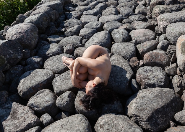 Jonge mooie naakte vrouw die zich voordeed op een stenen golfbreker. Naakte brunette geniet van de natuur