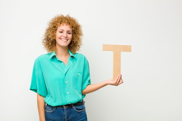 Jonge mooie opgewonden vrouw, gelukkig, blij, met de letter T van het alfabet om een woord of een zin te vormen.