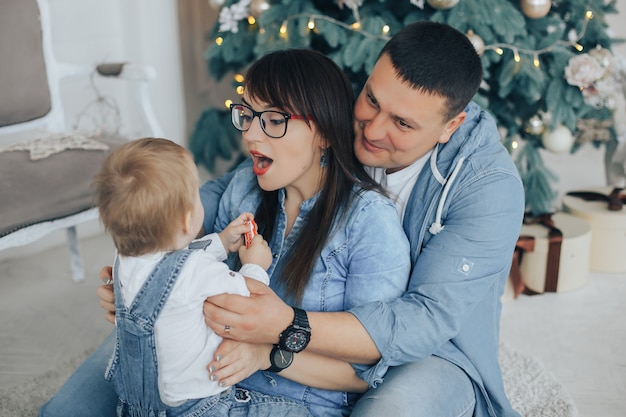 Jonge mooie ouders houden hun kleine schattige zoon in hun armen in de buurt van de kerstboom