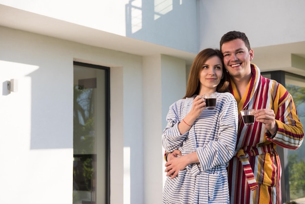 Jonge mooie paar in badjassen genieten van koffie in de ochtend voor hun luxe huis villa