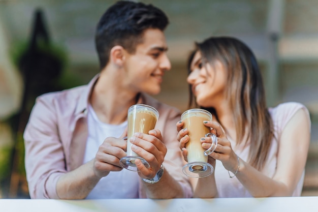 Jonge mooie paar praten op het terras in casual kleding met latte in hun handen