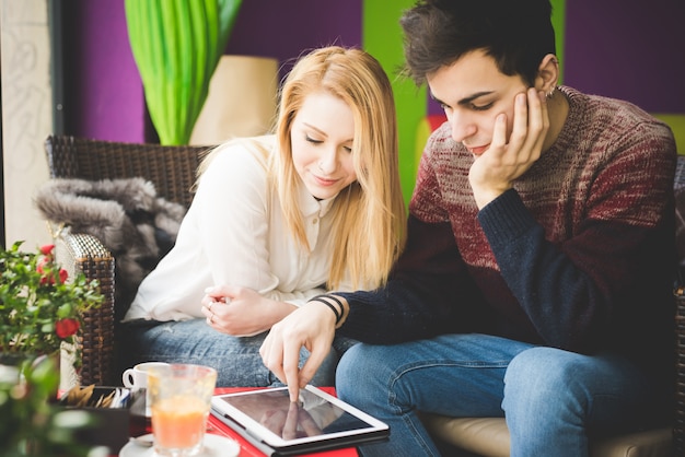 jonge mooie paarminnaars die bij de bar zitten die draadloze tablet gebruiken