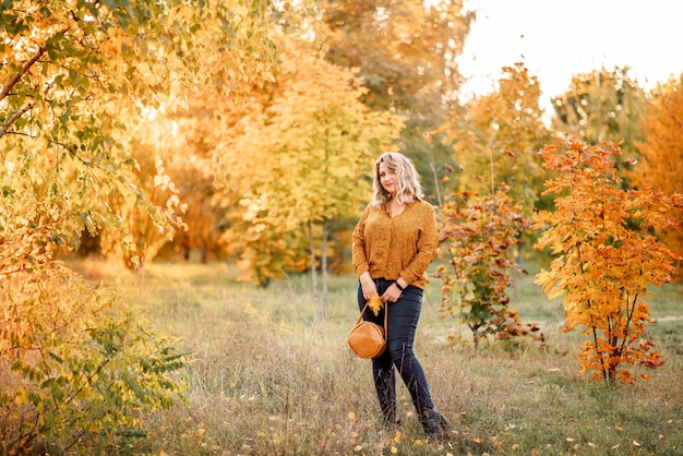 Jonge mooie plussize vrouw in een oranje shirt en spijkerbroek loopt in een herfstpark Mooie zonnige dag en natuur