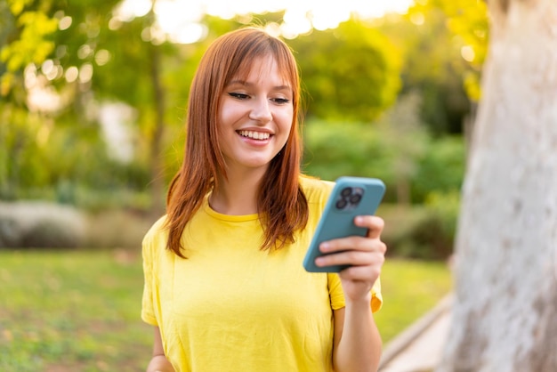 Jonge mooie roodharige vrouw buitenshuis die een bericht of e-mail verzendt met de mobiel