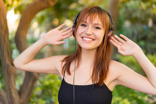 Jonge mooie roodharige vrouw die buitenshuis naar muziek luistert