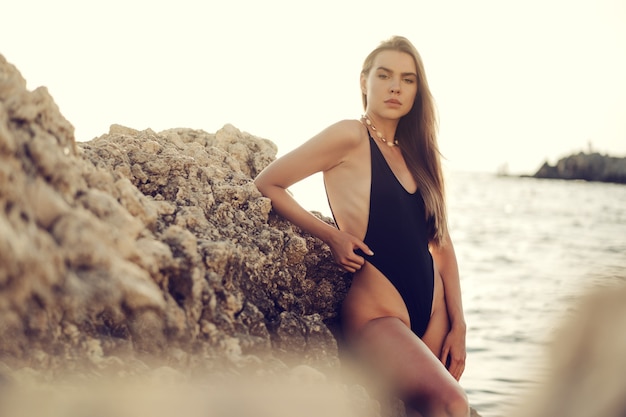 Jonge mooie sexy vrouwelijke model in zwarte bikini staande in zee in de buurt van enorme rots