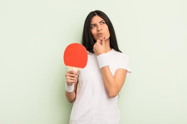 Jonge mooie Spaanse vrouw die denkt twijfelachtig en verward pingpongconcept te voelen