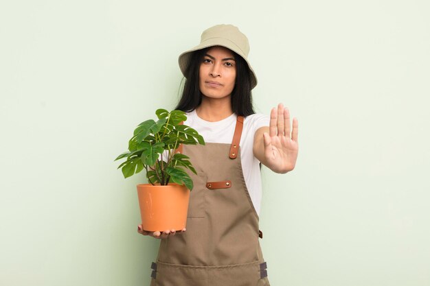 Jonge mooie Spaanse vrouw die er serieus uitziet en open palm toont die een stopgebaar maakt, boer of tuinmanconcept
