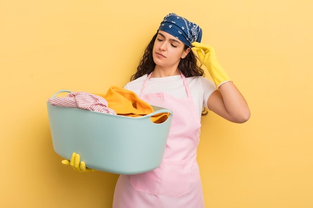 Jonge mooie Spaanse vrouw die gelukkig glimlacht en dagdroomt of twijfelt aan was- en kledingconcept