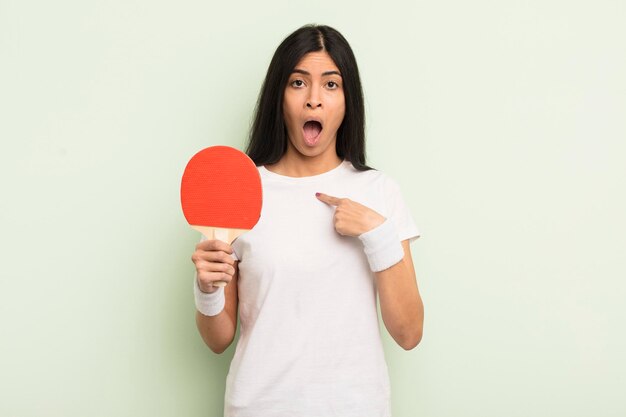 Jonge mooie Spaanse vrouw die geschokt en verrast kijkt met wijd open mond wijzend naar zelf ping pong concept
