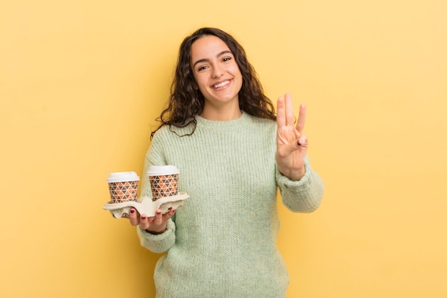 Jonge mooie Spaanse vrouw die lacht en er vriendelijk uitziet met nummer drie om koffieconcept mee te nemen