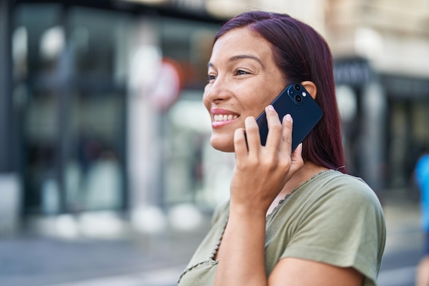 Jonge mooie Spaanse vrouw die lacht zelfverzekerd praten op de smartphone op straat