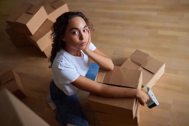 Jonge mooie spaanse vrouw die lacht zelfverzekerde kartonnen doos inpakken in nieuw huis