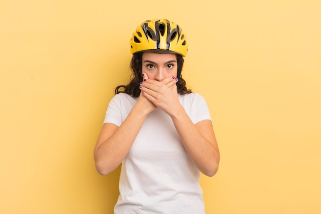 Jonge mooie Spaanse vrouw die mond bedekt met handen met een geschokt fietsconcept