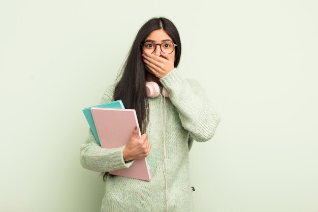 Jonge mooie Spaanse vrouw die mond bedekt met handen met een geschokt studentenconcept