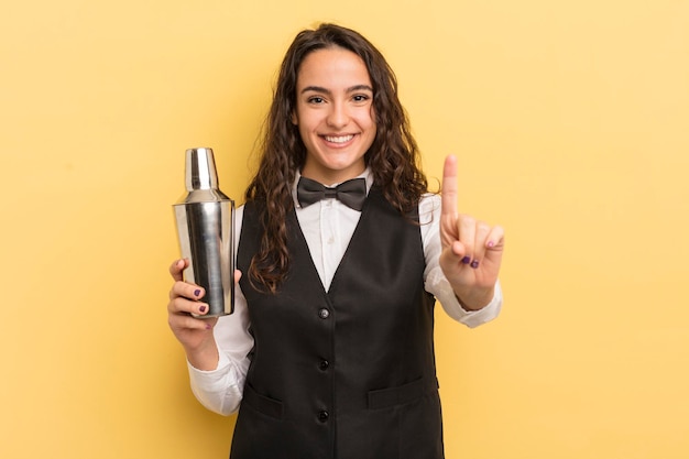 Jonge mooie Spaanse vrouw die trots en vol vertrouwen glimlacht en nummer één barman en cocktailconcept maakt