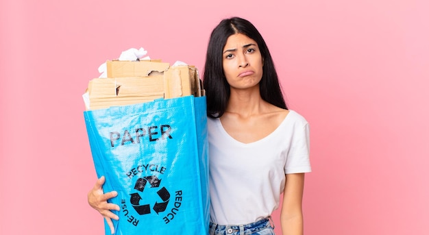Jonge mooie Spaanse vrouw die verdrietig en zeurt met een ongelukkige blik en huilt en een papieren zak vasthoudt om te recyclen