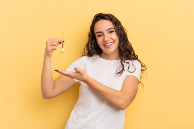 Jonge mooie Spaanse vrouw die vrolijk lacht en zich gelukkig voelt en een concept thermometer toont