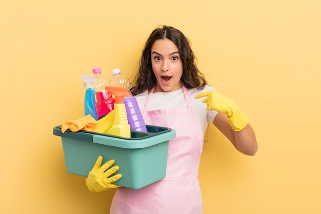 Jonge mooie Spaanse vrouw die zich gelukkig voelt en naar zichzelf wijst met een opgewonden huishoudelijk werk en een concept voor schone producten