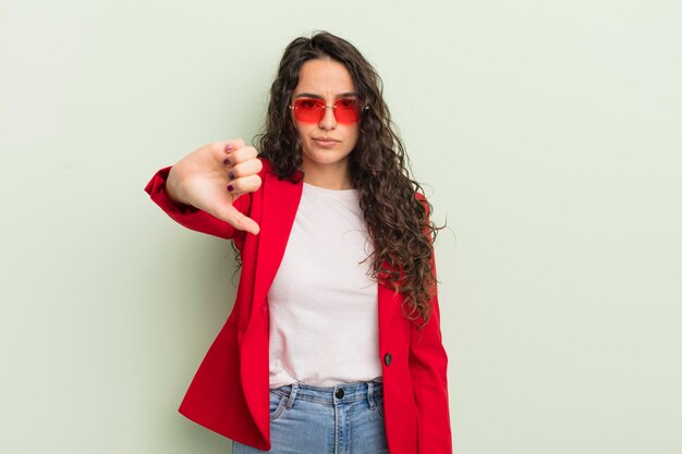 Jonge, mooie Spaanse vrouw die zich over het hoofd voelt en duimen naar beneden laat zien, coole zakenvrouw