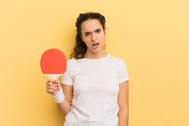 Jonge mooie Spaanse vrouw die zich verbaasd en verward pingpongconcept voelt