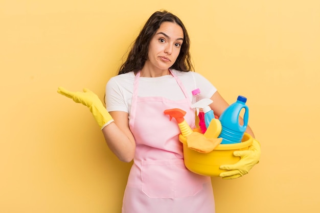 Jonge mooie Spaanse vrouw die zich verward en verward voelt en twijfelt aan huishoudelijk werk en een concept voor schone producten