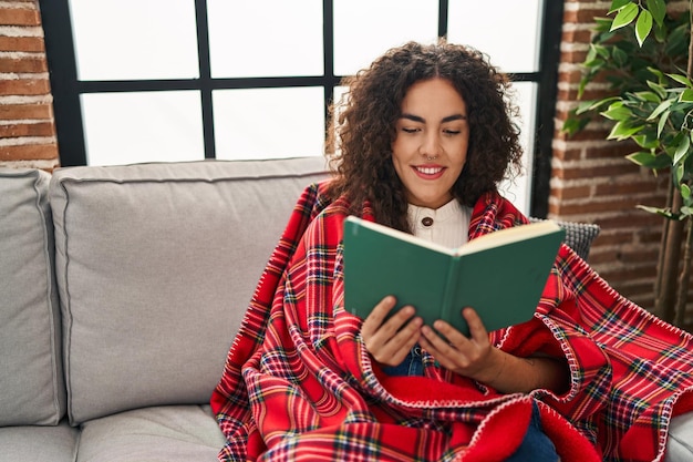 Jonge mooie Spaanse vrouw leesboek bedekking met deken thuis