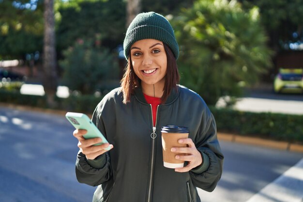Jonge mooie Spaanse vrouw met behulp van smartphone koffie drinken op straat