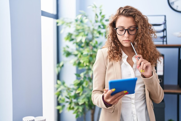 Jonge mooie Spaanse vrouw zakelijke werknemer met behulp van touchpad met ernstige uitdrukking op kantoor