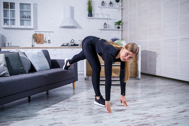 Jonge mooie sport meisje in legging en een top doet oefeningen thuis op de bank. Gezonde levensstijl. De vrouw gaat thuis sporten.